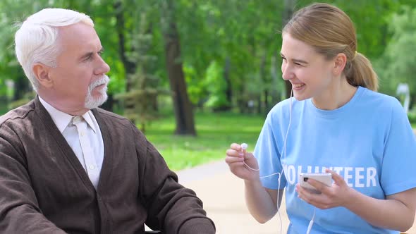 Female Volunteer Giving Headphone to Old Lonely Man, Listening to Music in Park