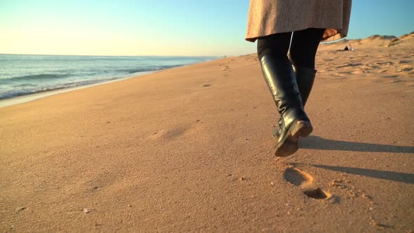 Woman Figure Shown From the Waist Down Walking Along the Beach Shore Wearing Long Boots