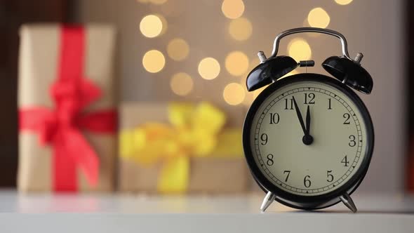 Vintage black alarm clock on a table with gifts on background