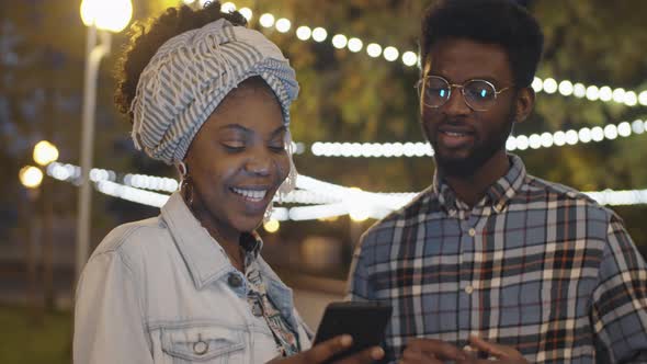 Afro Friends Using Smartphone and Chatting Outdoors in Evening