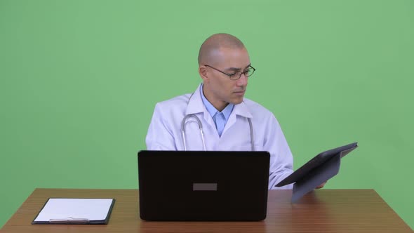 Busy Bald Multi Ethnic Man Doctor Multitasking at Work Behind Desk