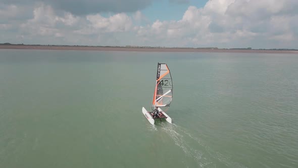 Man sailing his catamaran in the sea. Drone pans to the side, beautiful coastal landscape.