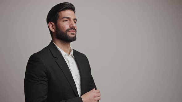 Alluring Handsome Bearded Cuban Guy with Dark Hair Corrects His Black Suit Tuxedo's Wristband Over