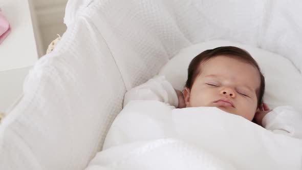 Baby girl sleeping in bassinet, with baby clothes beside