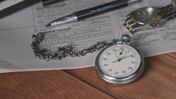 Vintage Stopwatch Lies on Wooden Desk with Old Documents and Counts Seconds