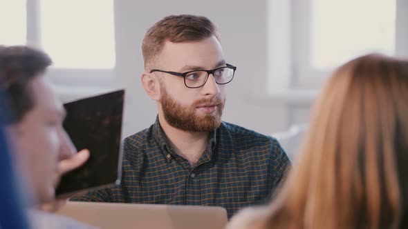 Medium Shot of Young Professional Caucasian Businessman Talking To Colleagues Behind Table