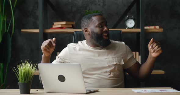 Happy African Businessman Dancing Cheerfully While Working at Laptop in Home Office