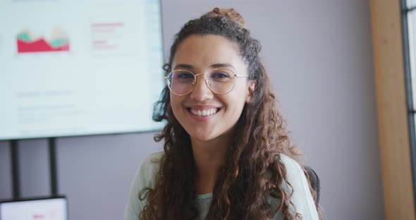 Portrait of smiling biracial businesswoman wearing glasses in meeting room with screen in background