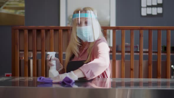 Senior Cafe Owner in Protective Mask and Gloves Clean Counter with Spray