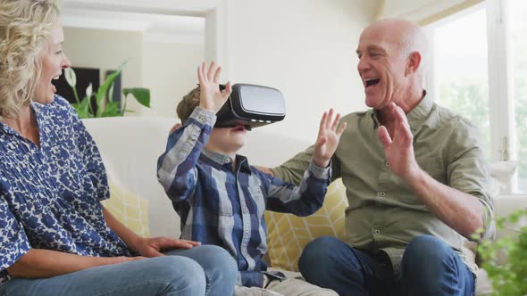 Happy senior caucasian couple with grandson using vr headset in living room