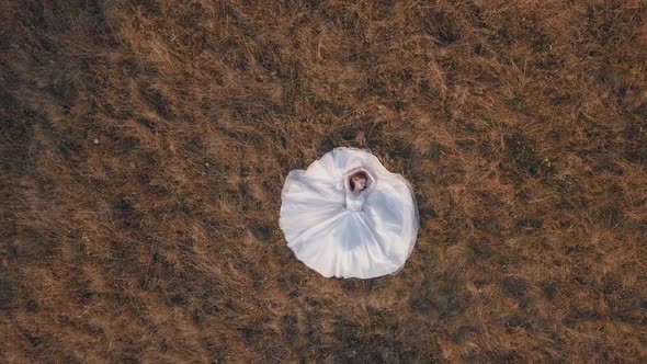 Beautiful and Lovely Bride in Wedding Dress Lie on Grass on Field. Aerial View