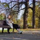 A Young Woman Sits on a Bench in an Autumn Park and Looks at the Beautiful Yellow Foliage - VideoHive Item for Sale