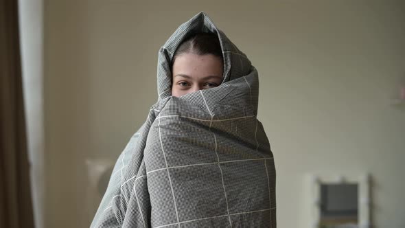 smiling and funny woman wrapped in a blanket in the morning after waking up