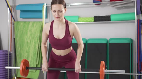 a Beautiful and Slender Young Woman Does Exercises with Dumbbells in the Gym