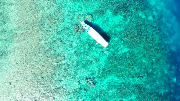 Top view of long boat floating over calm crystal water of turquoise lagoon over coral reefs and rock