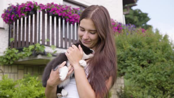A Young Beautiful Caucasian Woman Plays with a Cute Little Puppy in Her Arms in a Rural Area