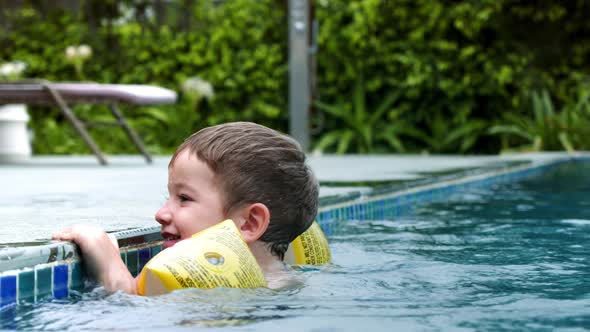 Lttle Boy in His Pool with Inflatable Armlets on His Hands Hold on to the Side of the Pool with His