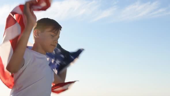 Blonde Boy Waving National USA Flag Outdoors Over Blue Sky at the River Bank