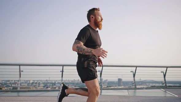 Bearded Athlete Runs on Footbridge Against City Panorama