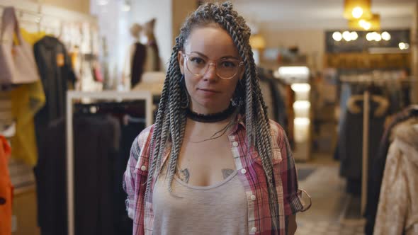 Young Woman with Braids Standing Near Rack with Dresses in Clothes Shop