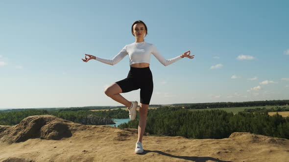 Slender Woman in White Top and Black Sports Shorts Practices Yoga Outdoors in Nature