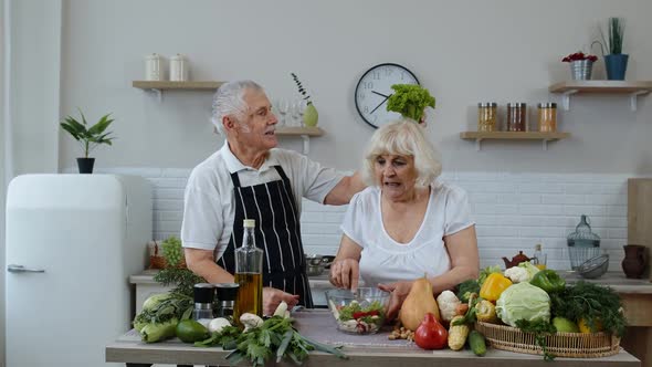 Senior Grandparents in Kitchen. Funny Grandpa Joking on Grandma. Putting a Lettuce About Her Head