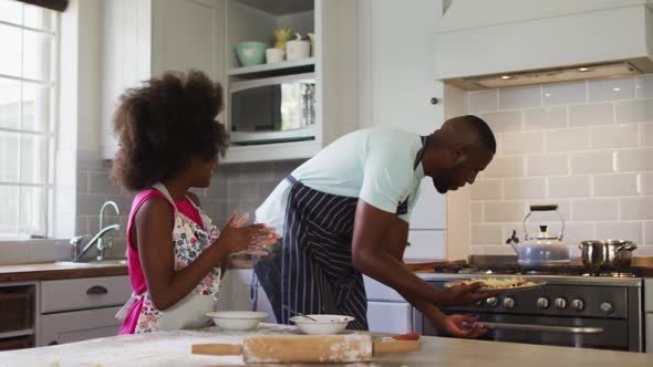 African american daughter and her father making pizza together in kitchen