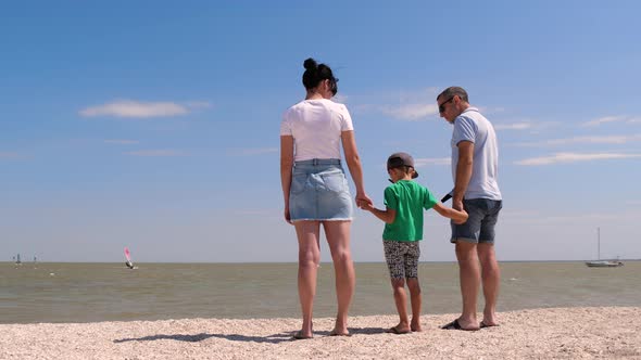 A Father and Mother Hold Their Son's Hands While Standing on the Edge of the Sea. A Happy Family