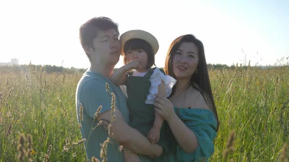 Korean Family with Their Daughter Lie in a Field in the Grass at Sunset