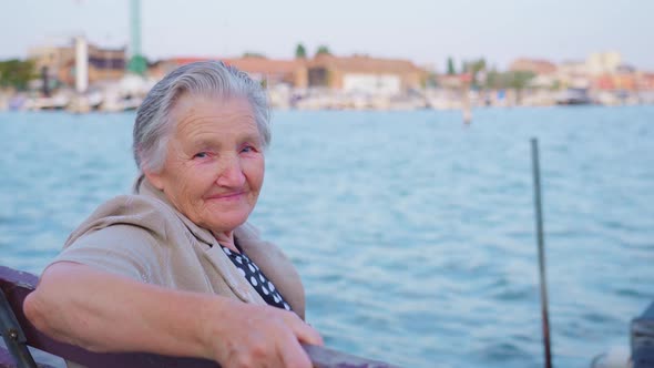 Elderly Woman Traveler Sits on Embankment of Chioggia