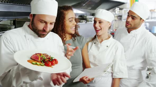 Team of chefs holding food plate in commercial kitchen