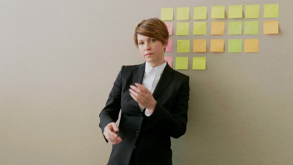 Successful businesswoman leaning on office wall with adhesive notes