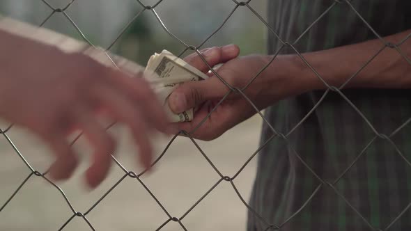 Close-up of Male African American and Caucasian Hands Passing Money and Pills Through Mesh Fence