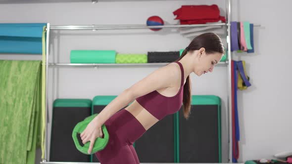 a Beautiful and Slender Young Woman Does Exercises with Weights in the Gym