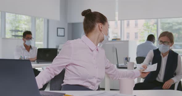 Businesswoman in Safety Mask Working at Desk in Office Take Documents From Colleague