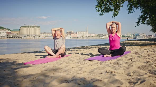 Senior Man and Woman Sit in Yoga Pose with Hands Behind Head