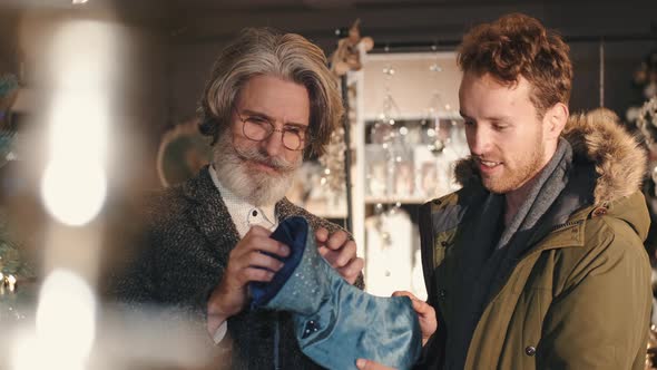 Mature Man Holding Blue Stocking Standing with Grandson in a Shop