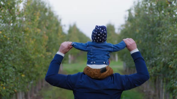 Male Parent with Small Male Child Around His Neck Having Fun Playing Outdoors Among Trees in Park