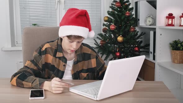 A Teenage Boy in Santa Hat Hangs Online Shopping Using a Laptop