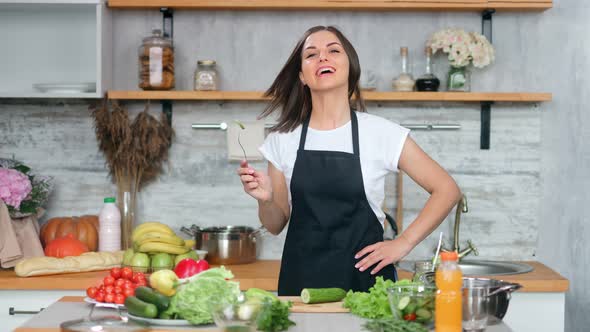 Smiling Young Housewife in Apron Trying Cucumber Dancing Cooking Healthy Food at Cozy Kitchen