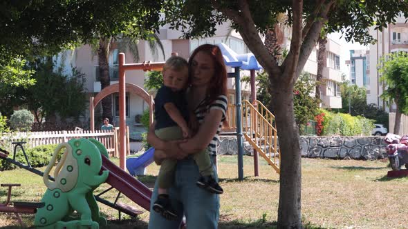 Ginger Woman Mother Holding Her Baby and Walks in the Park