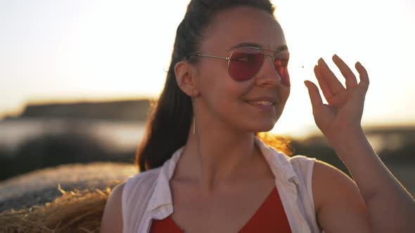 Beautiful Young Woman Putting Down Sunglasses Looking at Camera Standing in Sunrays at Golden Sunset
