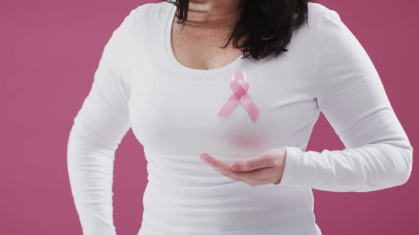 Mid section of woman with pink ribbon on her chest holding invisible object against pink background