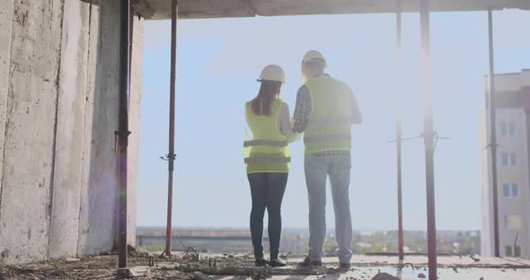 Back Turned Architect and Technician at Construction Site Reviewing Office Blueprints