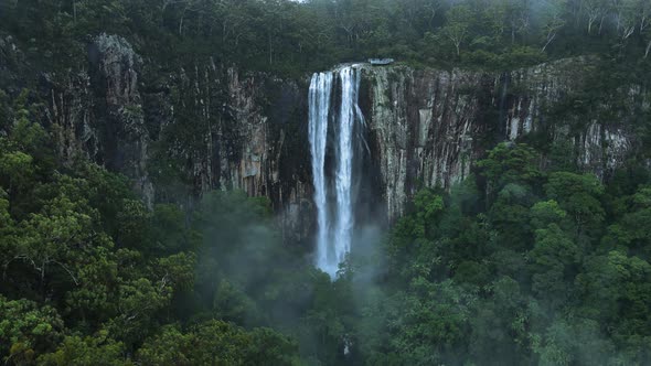 A majestic waterfall cascading over a lush tropical rainforest mountain scenery. Panoramic high dron