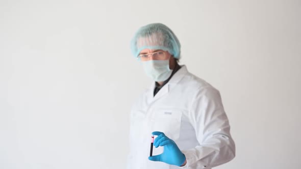 Portrait of a Doctor in a White Coat and Protective Mask Shows a Sample of Blood and Shows Thumb