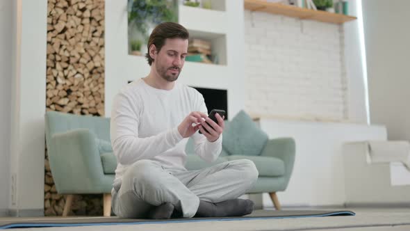 Young Man Using Smartphone on Yoga Mat at Home