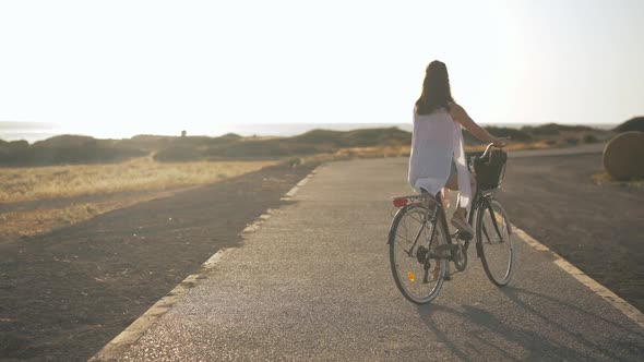 Back View Young Slim Woman Riding Bicycle in Slow Motion at Background of Cyprus Landscape at Sunset