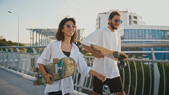Young Couple in Love Walking with Skateboards on Bridge Slow Motion
