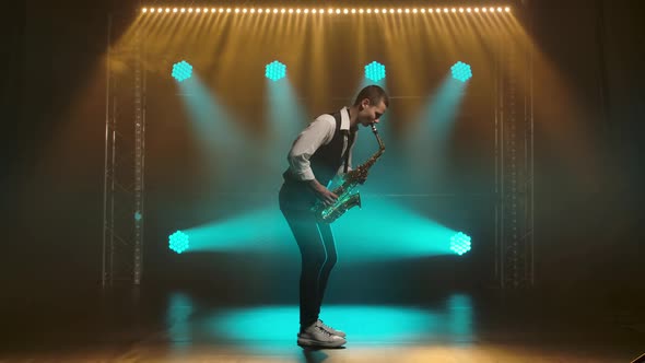 A Young Stylish Guy Plays the Golden Shiny Saxophone in the Turquoise Spotlights on Stage